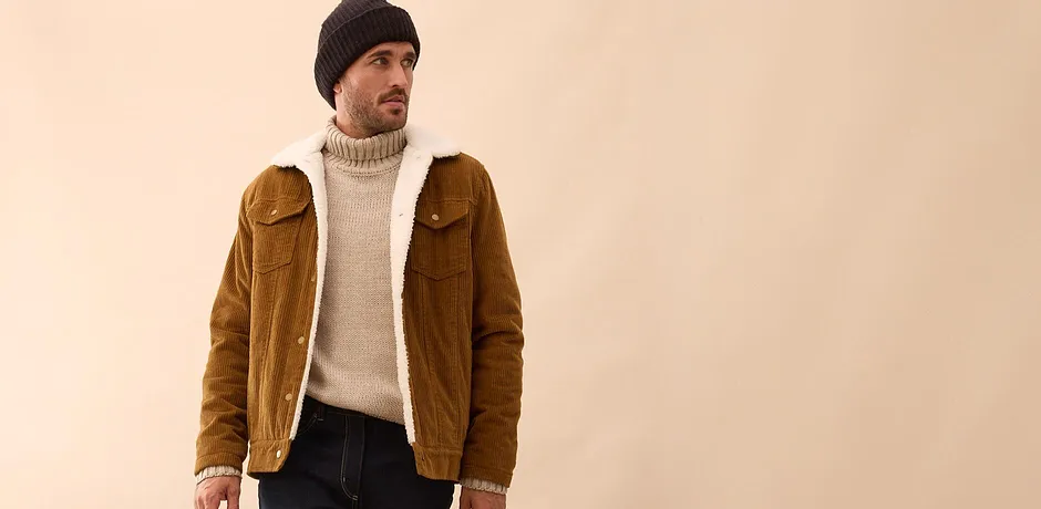 Bruine corduroy jas over crèmekleurige coltrui met donkere jeans en muts.