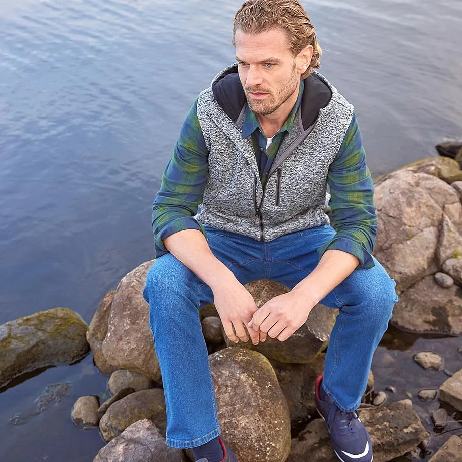 Bodywarmer met motief over groen overhemd gecombineerd met blauwe jeans.