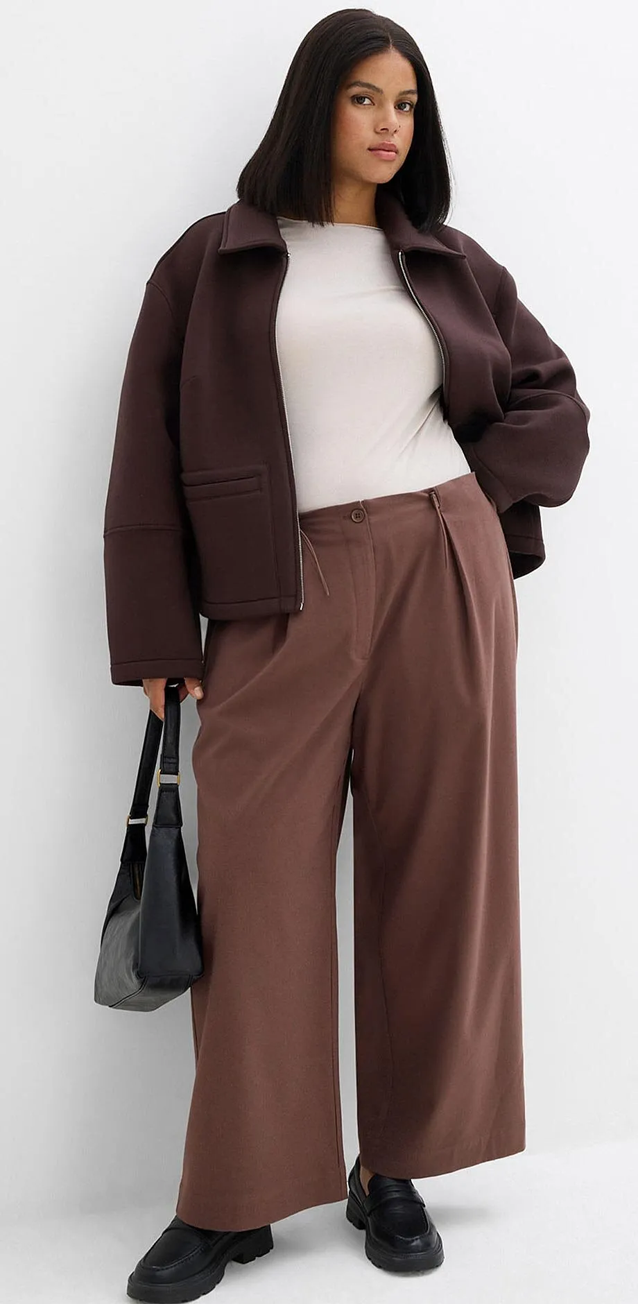 Bruine jas, witte top en wijde broek in aardetinten.