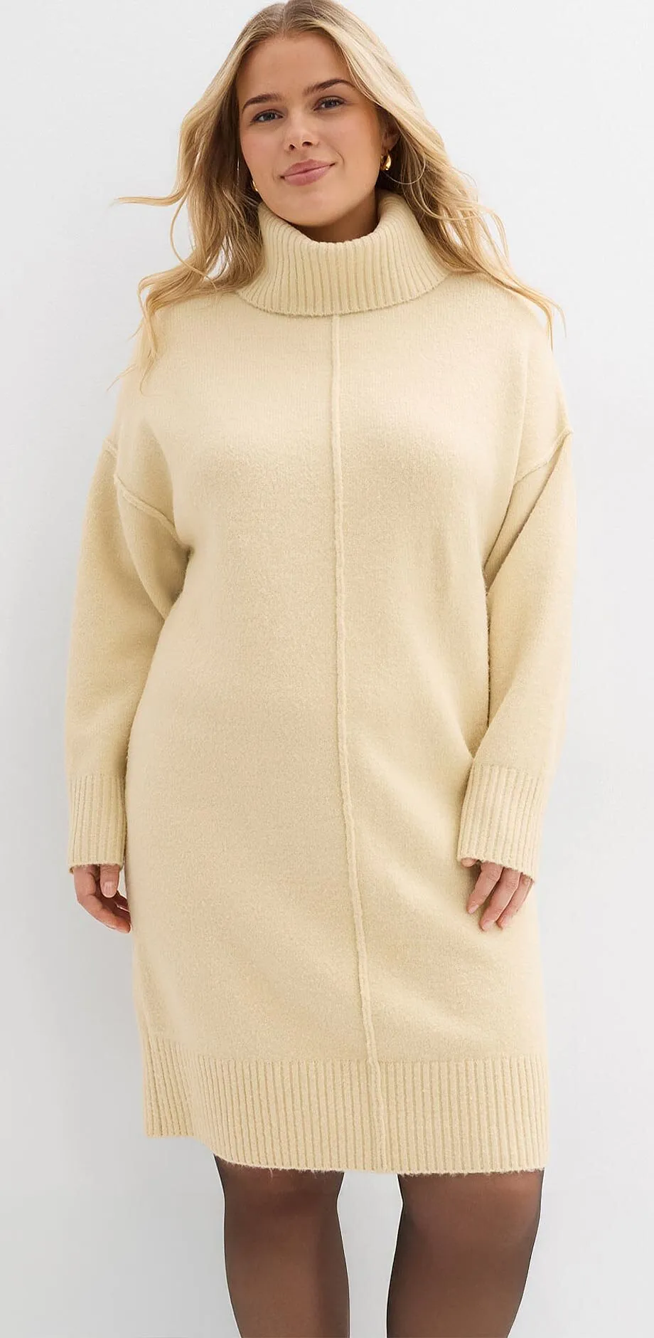 Crèmekleurige gebreide jurk met hoge kraag en lange mouwen.
