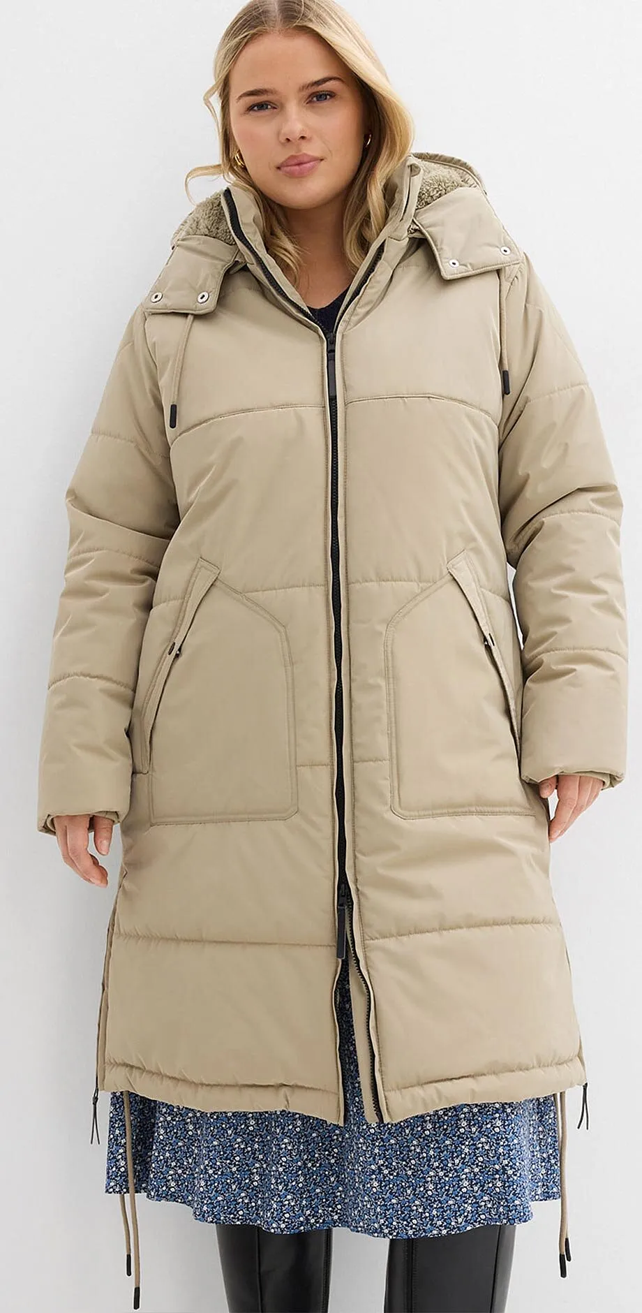 Beige gewatteerde jas met capuchon over blauwe bloemetjesjurk.