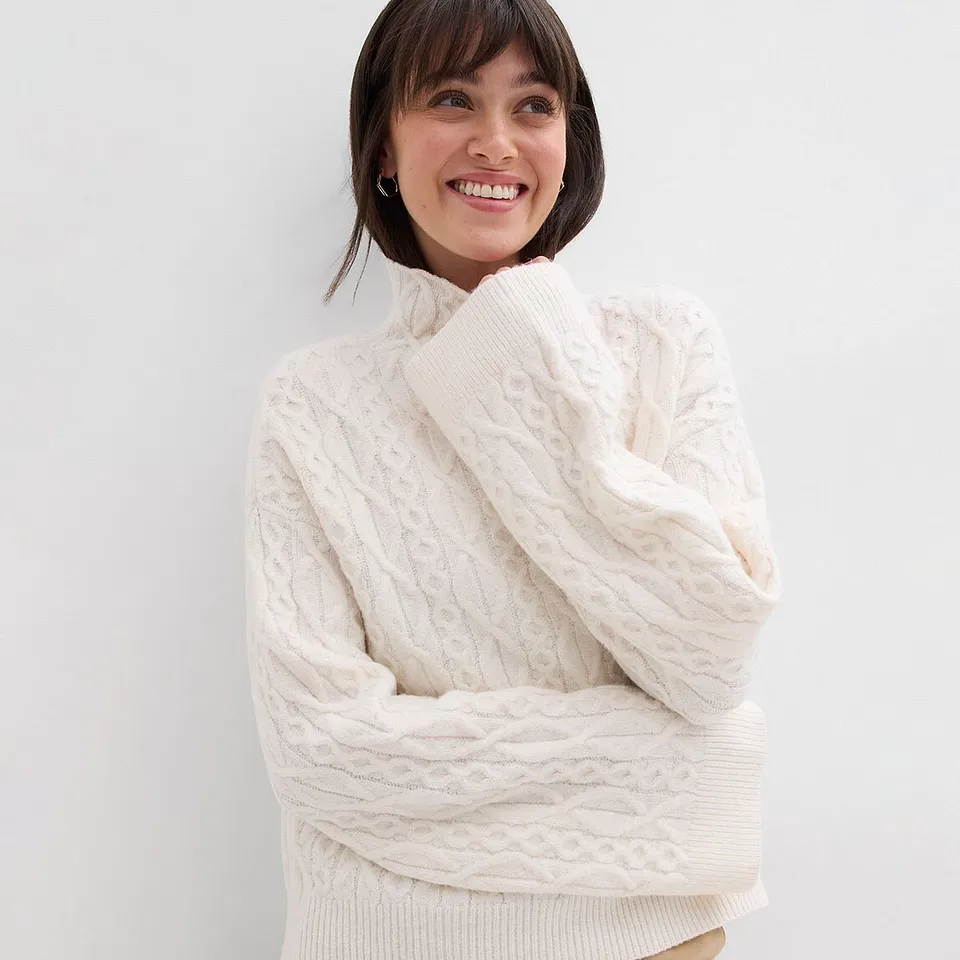 Witte gebreide trui met hoge kraag en kabelpatroon.