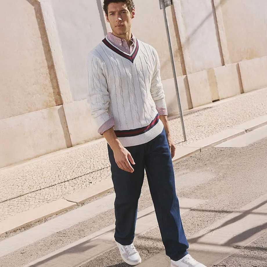 Witte trui met kabelpatroon, donkere broek en witte sneakers.