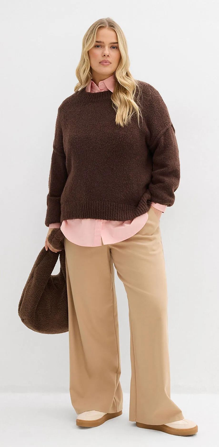 Bruine trui over roze overhemdblouse, beige broek en bruine handtas.