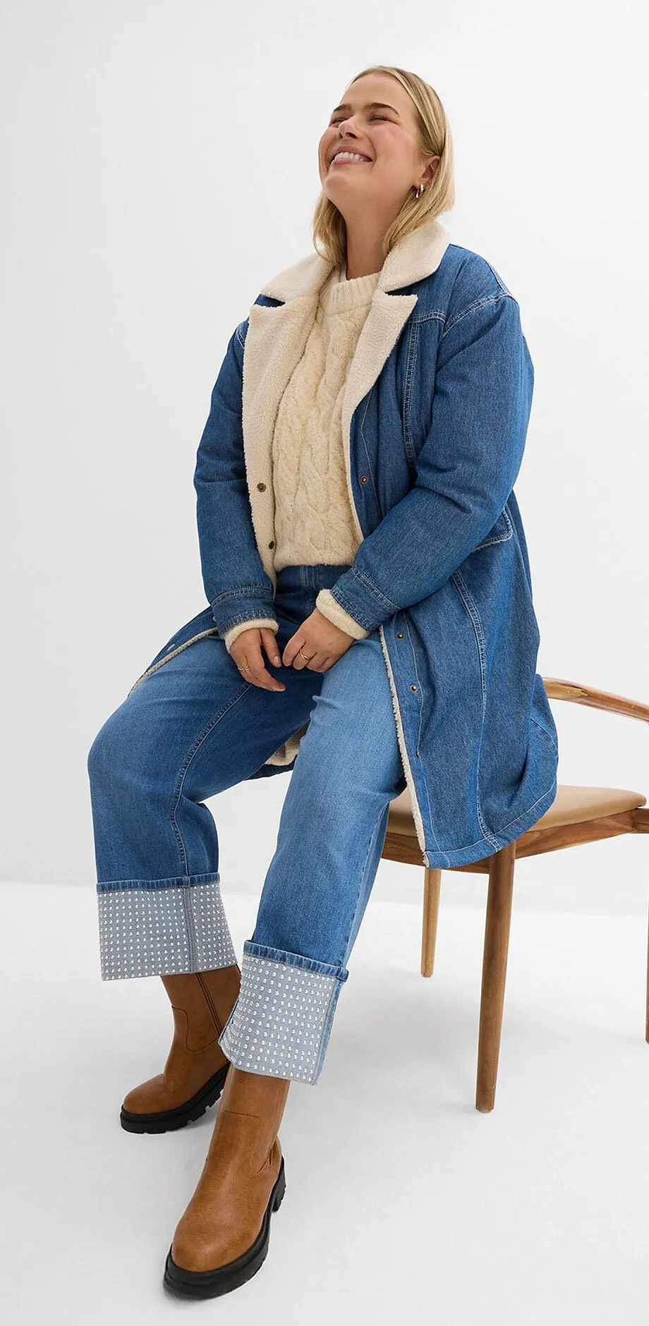 Jeanslook met lange jas, beige trui en jeans.