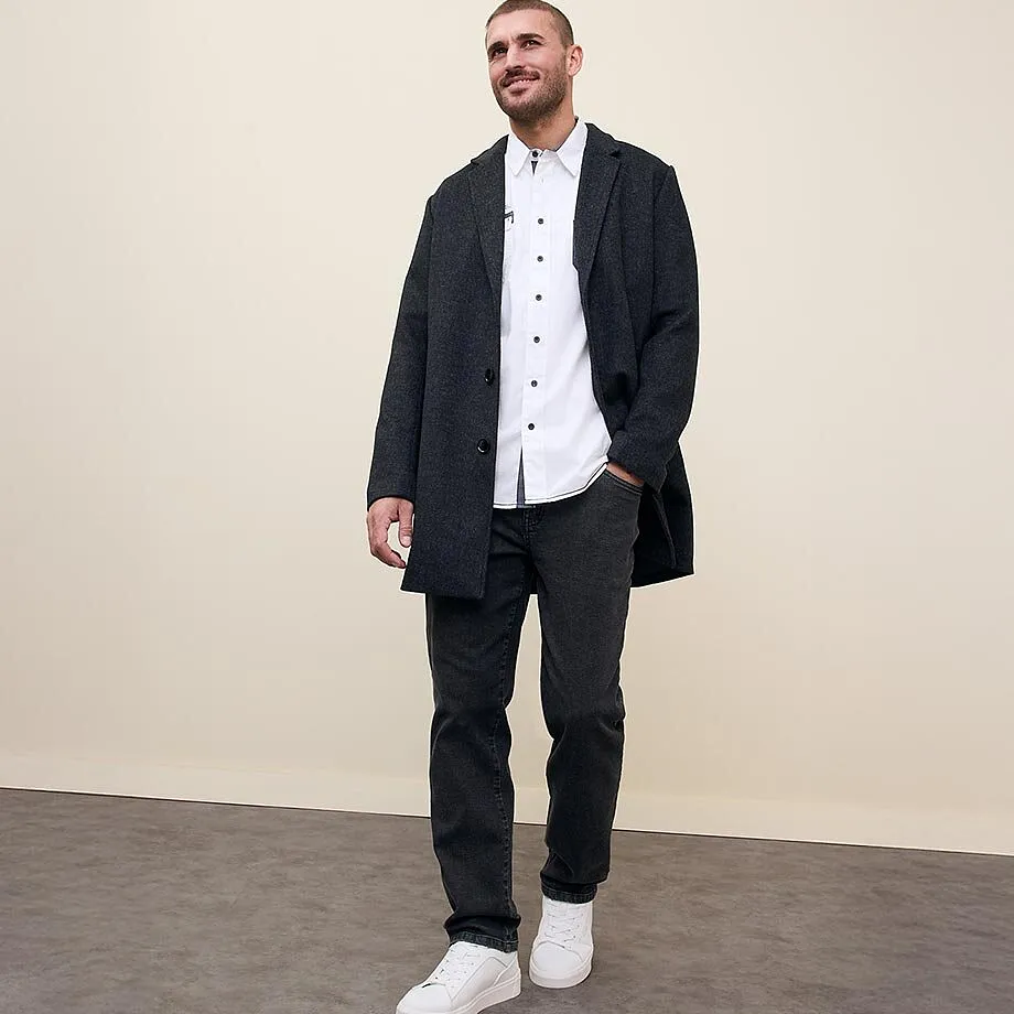Donkere lange jas over wit overhemd met bijpassende jeans en witte sneakers.