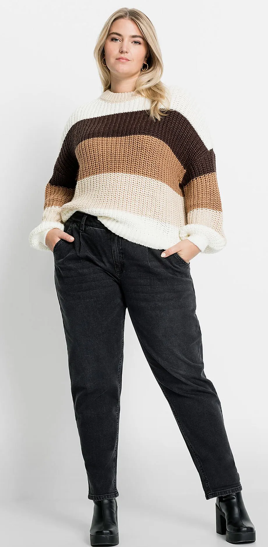 Gestreepte gebreide trui in aardetinten, gecombineerd met donkere jeans en zwarte schoenen.